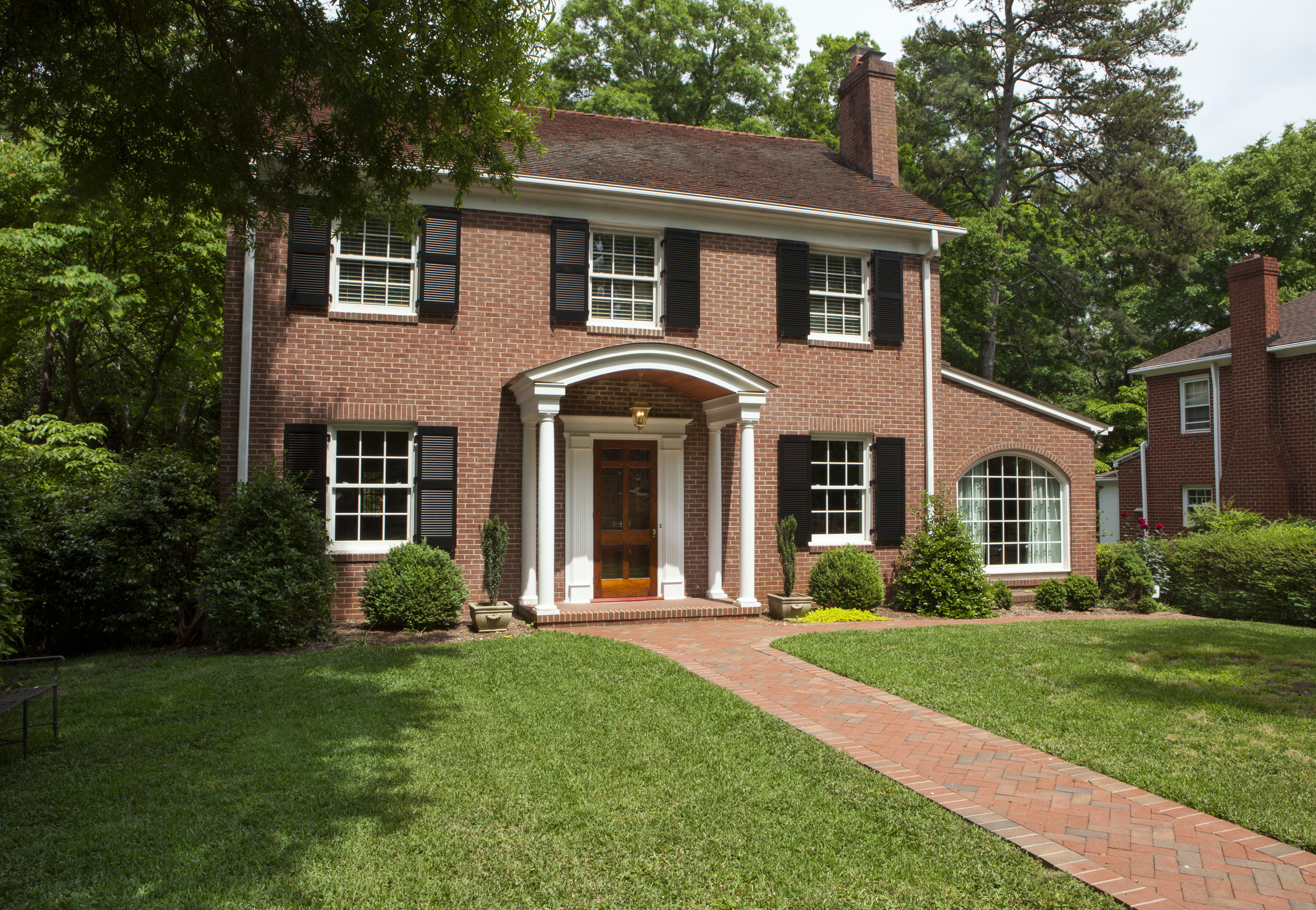 Traditional brick home in Myers Park with arched portico and maintenance-free shutters by Distinctive Design + Build + Remodel.