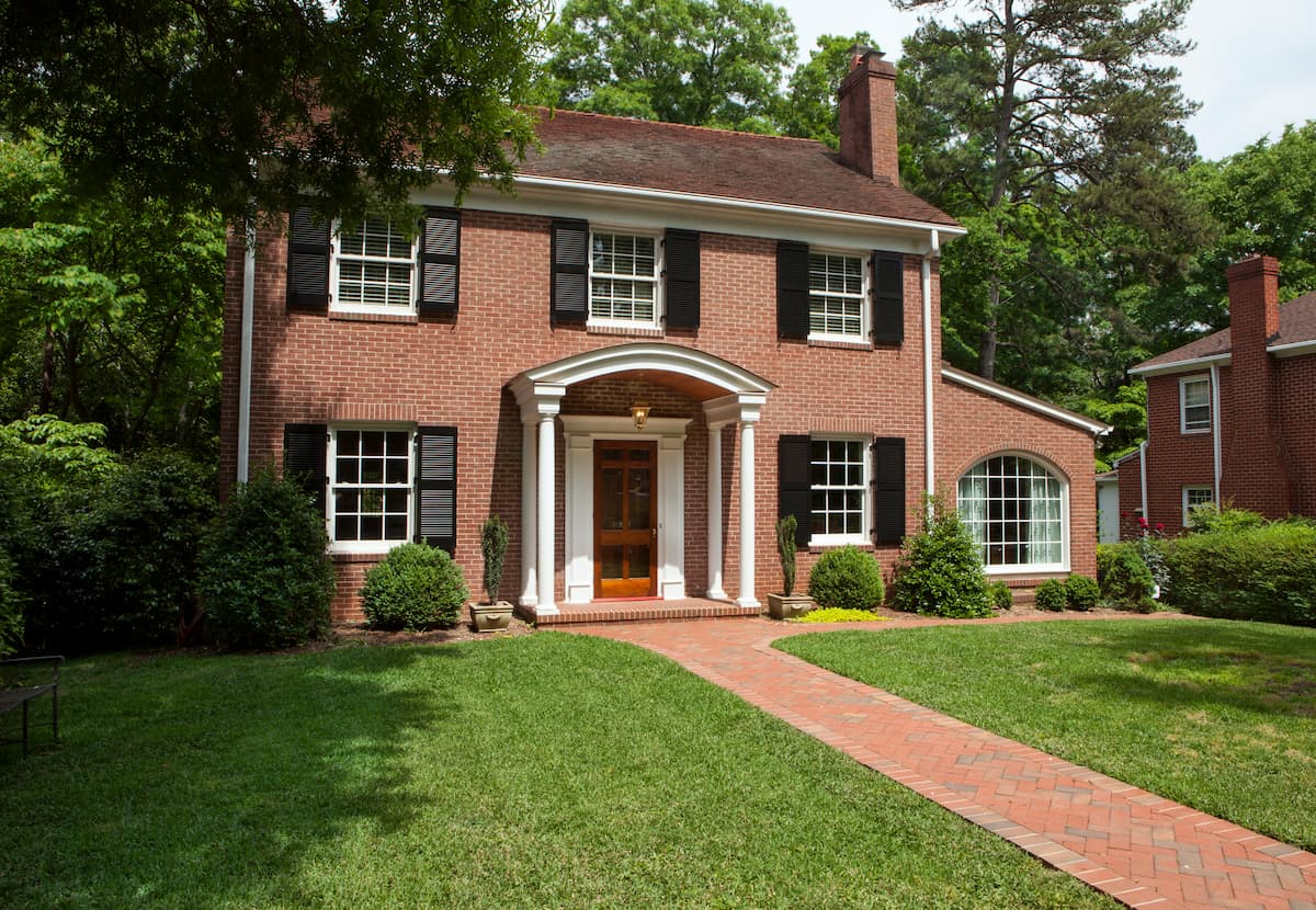 Traditional brick home in Myers Park with arched portico and maintenance-free shutters by Distinctive Design + Build + Remodel.