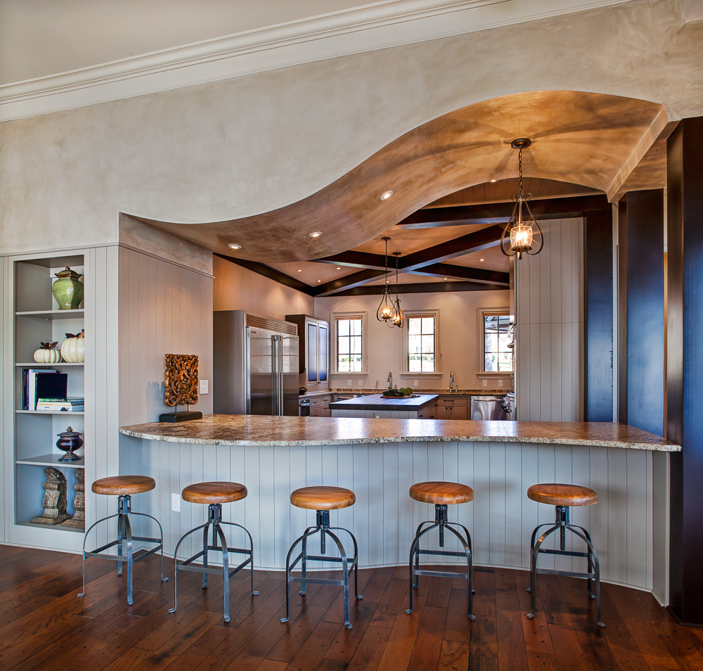A show-stopping kitchen remodel on Lake Norman by Distinctive Design + Build + Remodel with corbel ceiling, a curved seating bar, custom cabinetry and leathered granite countertops.