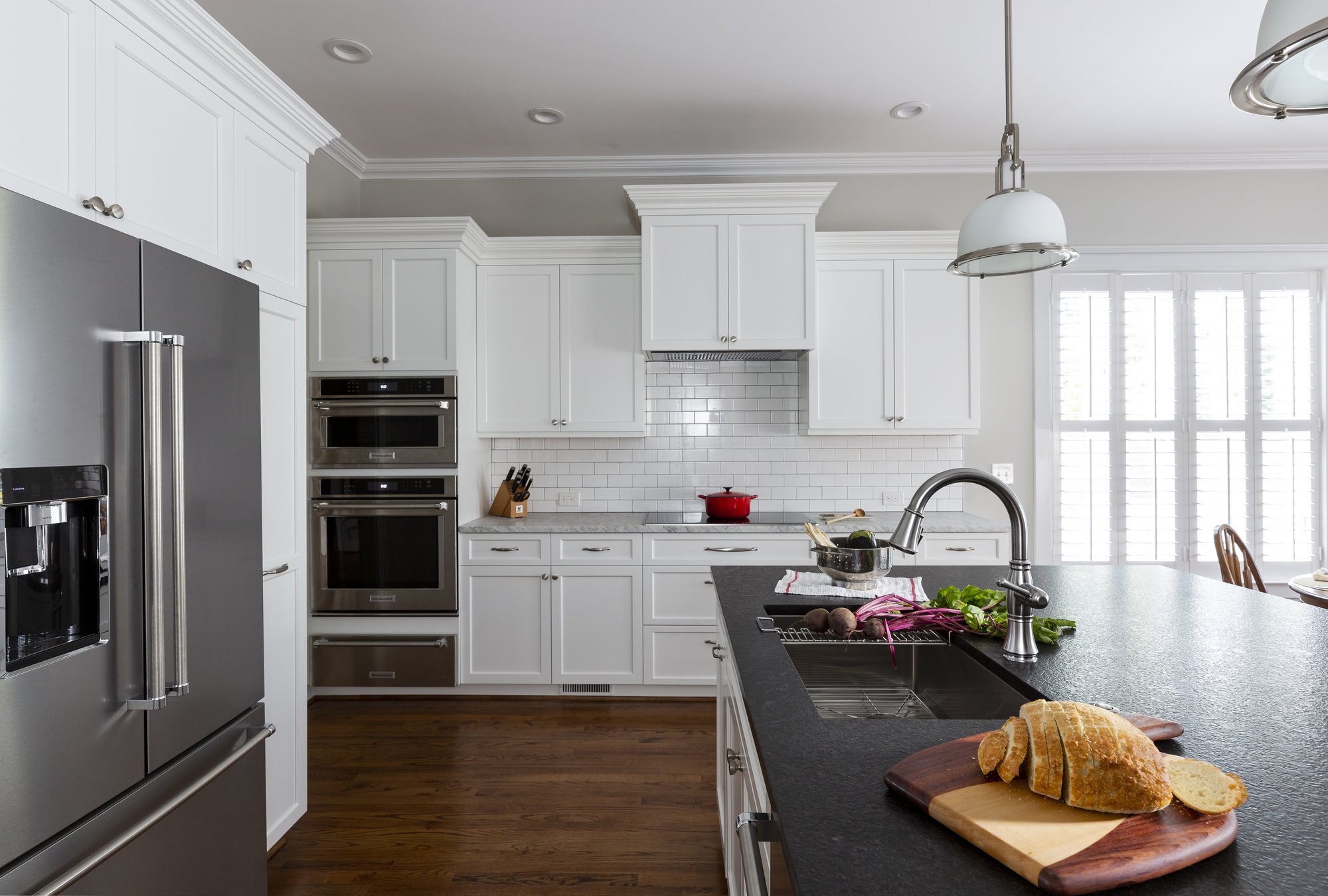 A boring builder-grade kitchen in Belmont, NC is transformed by Distinctive Design + Build + Remodel with crisp white cabinetry and subway tile, black leathered granite and stainless-steel appliances.