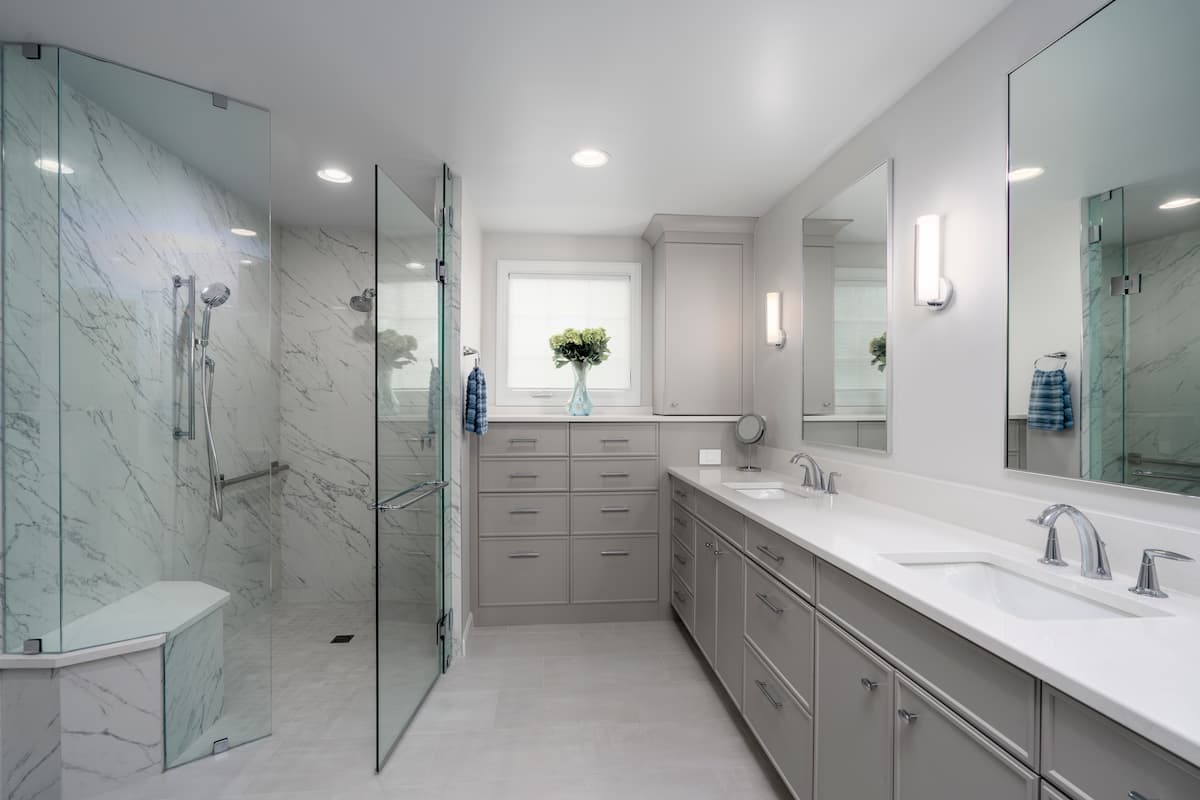 Primary bathroom remodel in Charlotte, NC with expansive gray cabinetry, curbless shower and heated floors by Distinctive Design + Build + Remodel.