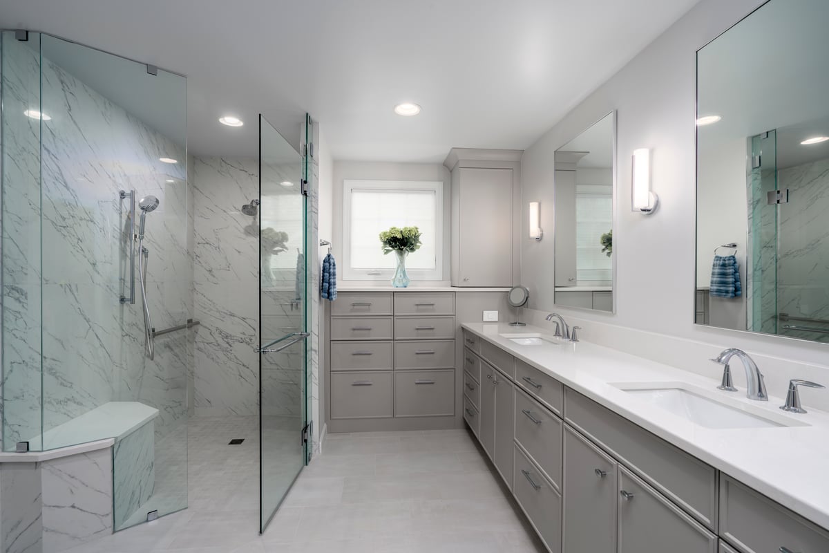 Primary bathroom remodel in Charlotte, NC with expansive gray cabinetry, curbless shower and heated floors by Distinctive Design + Build + Remodel.