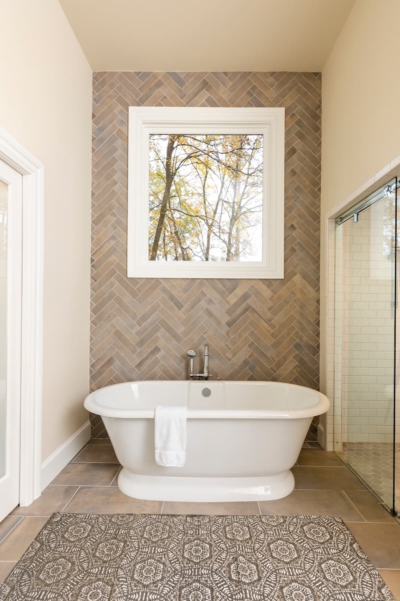 Free-standing tub with herringbone tile feature wall in a bathroom remodeled by Distinctive Design + Build + Remodel in Charlotte, NC