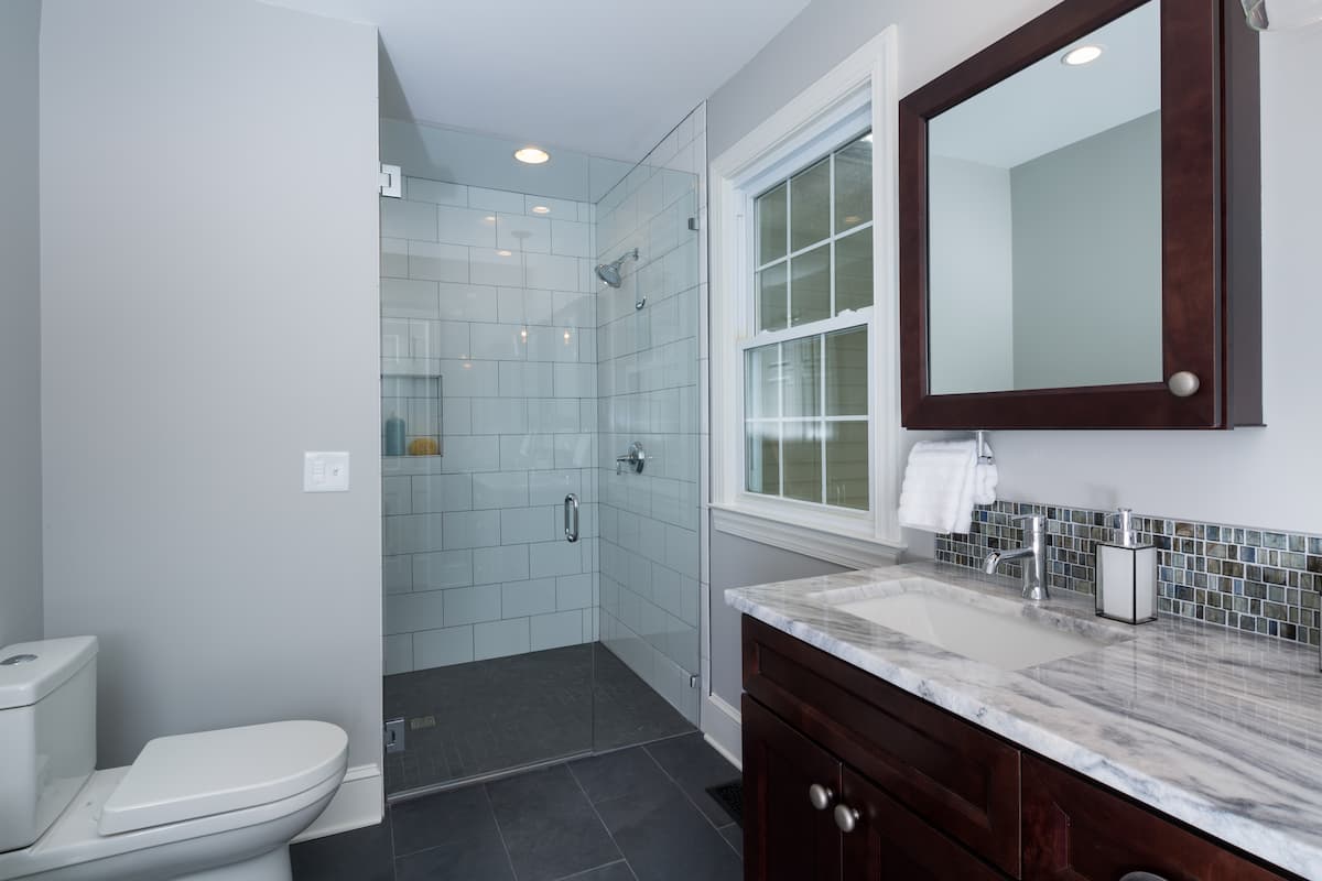 Bathroom remodel in Charlotte, NC with a curbless shower, large format gray floor tile, white tile on the shower walls a double vanity with a stone countertop.