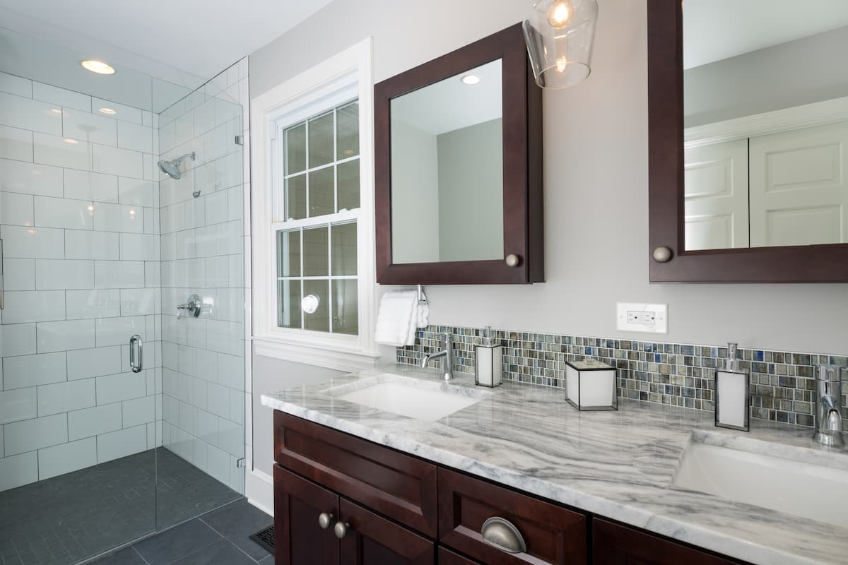 Bathroom remodel in Charlotte, NC with a curbless shower, large format gray floor tile, white tile on the shower walls a double vanity with a stone countertop.