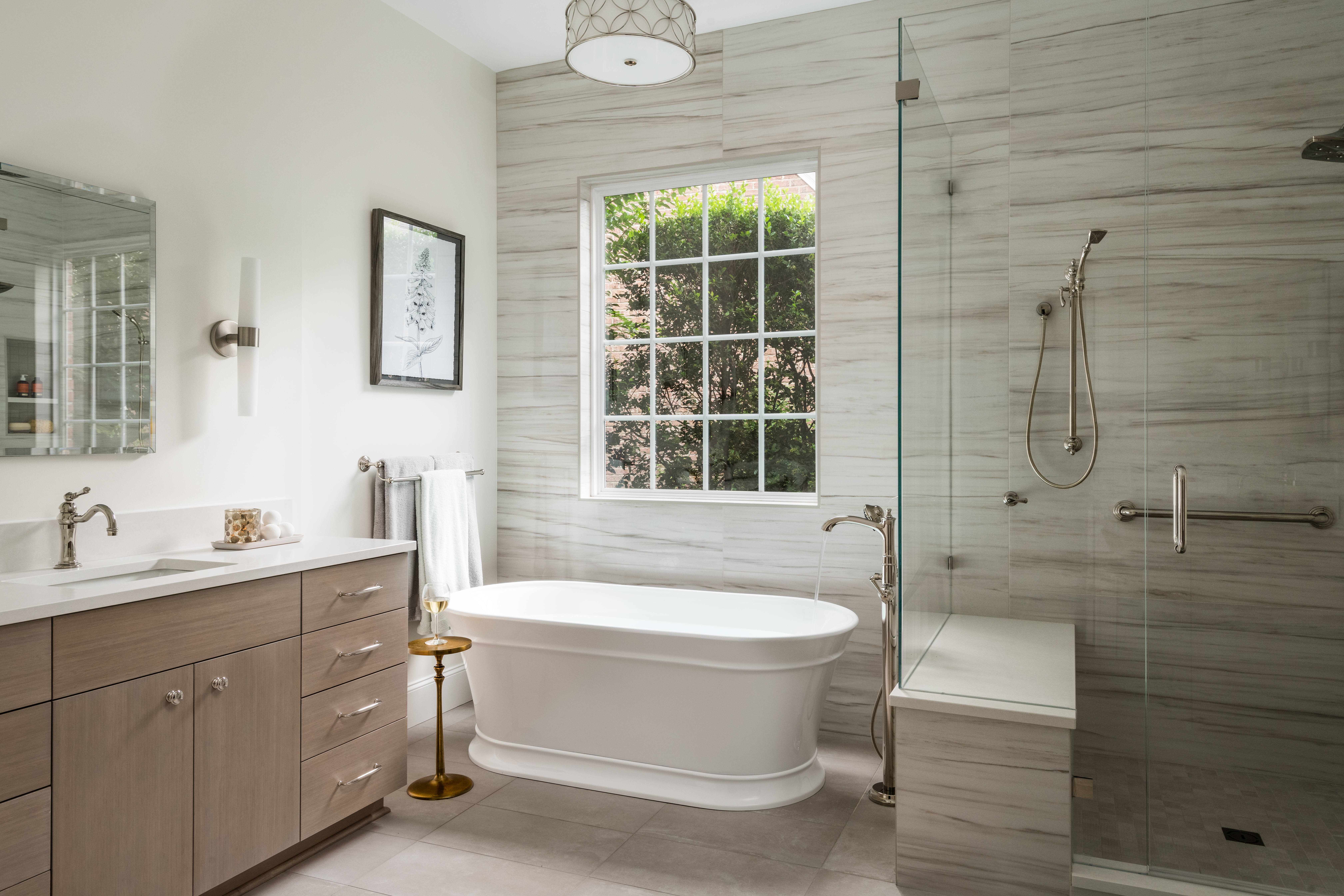 Primary bathroom in Ballantyne is transformed by Distinctive Design + Build + Remodel with bamboo cabinetry, free-standing tub, tile feature wall and chrome fixtures.