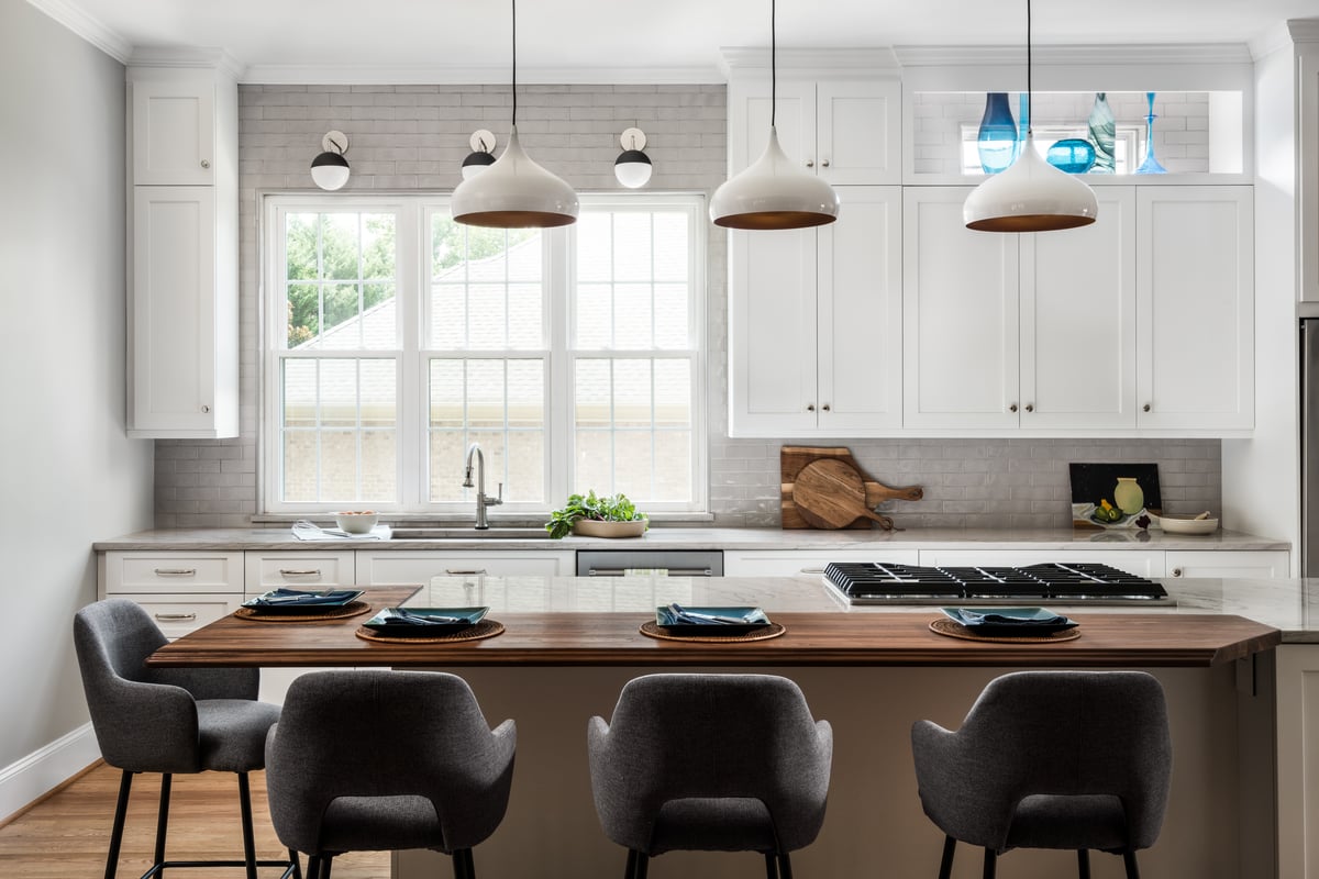 Kitchen after remodel in the Ballantyne neighborhood of Charlotte, NC with white cabinetry, white pendant lights and walnut seating bar by Distinctive Design + Build + Remodel.
