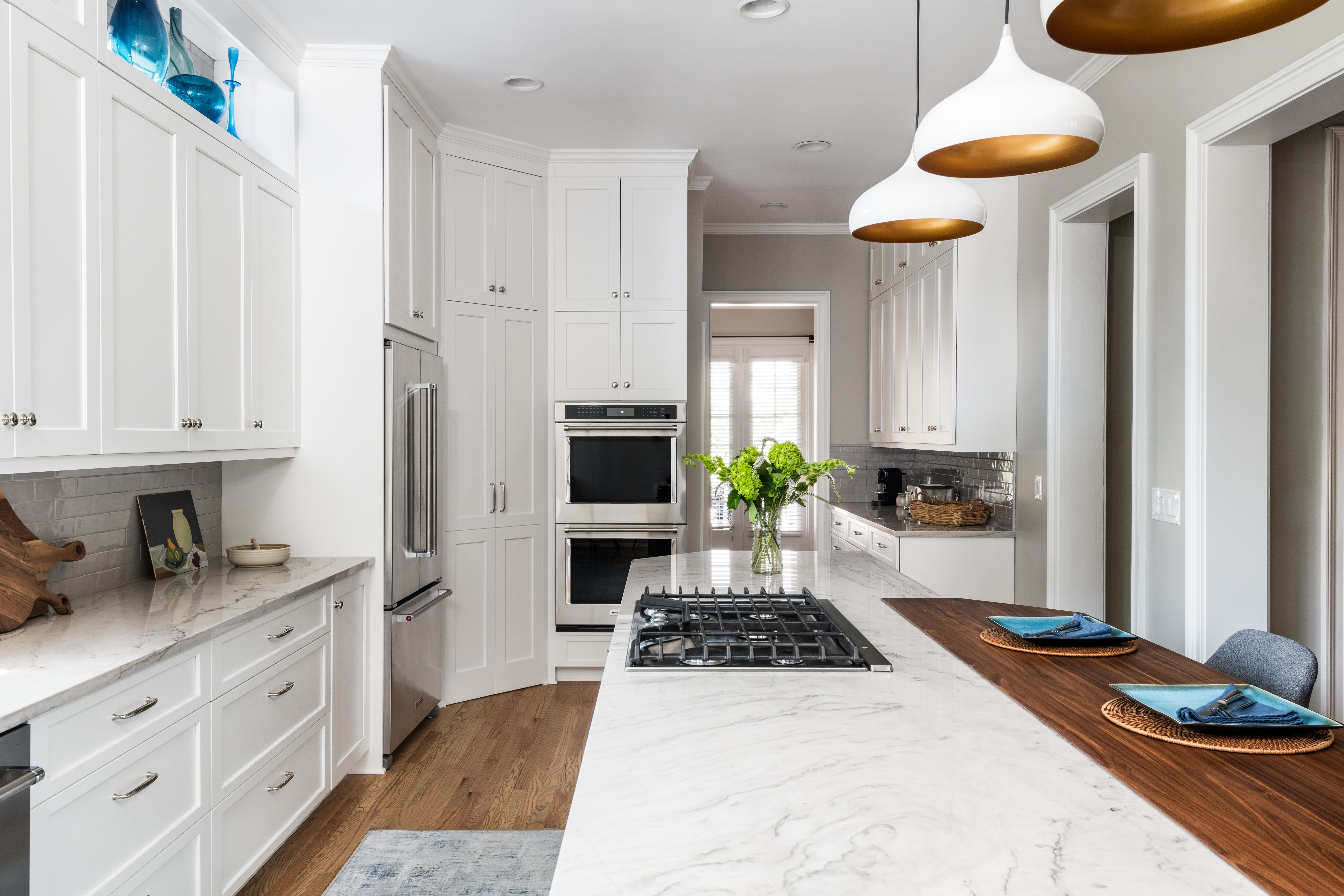 Remodeled kitchen in Charlotte, NC with quartzite countertops, white cabinetry and walnut seating bar by Distinctive Design + Build + Remodel.