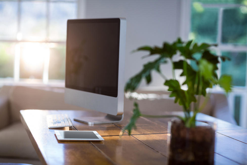 A computer and tablet on a wood table with a plant in a home office by Distinctive Design + Build + Remodel in Charlotte, NC.