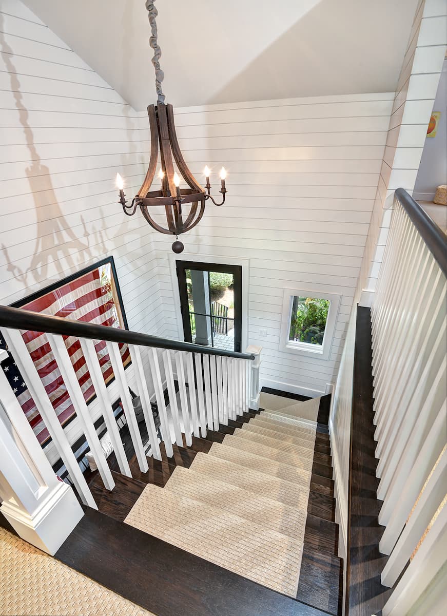 Relocated staircase in a whole house remodel by Distinctive Design + Build + Remodel on Kiawah Island with new railings, shiplap and chandelier.