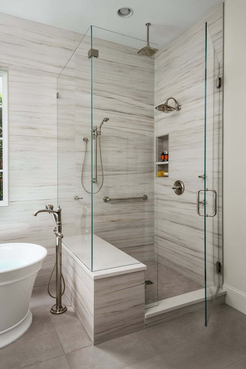 Shower with multiple shower heads, a deep niche, and bench in a master bathroom remodel by Distinctive Design + Build + Remodel in Charlotte, NC.