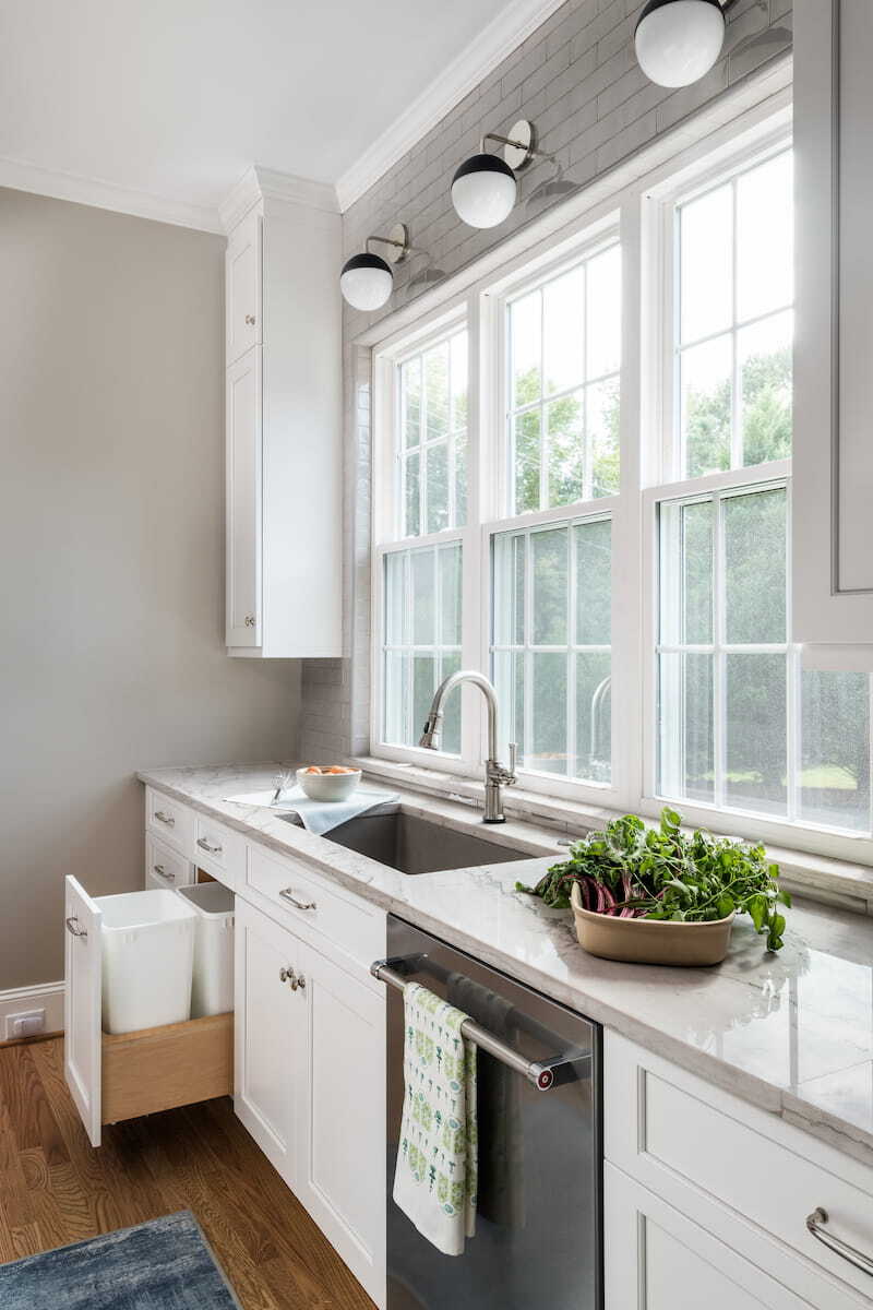 Double pull-out trash cans next to sink under a window in a kitchen remodel by Distinctive Design + Build + Remodel in Charlotte, NC.